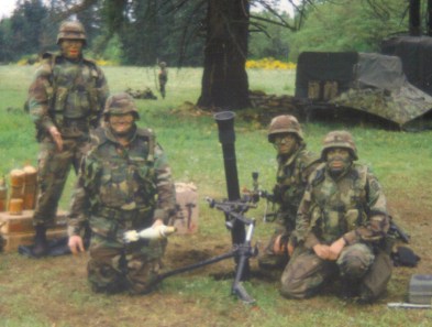 photo: four soldiers by a mortar tube. One hold a mortar round.